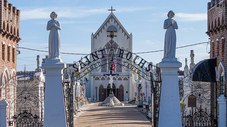 A chapel with a gated entrance, two human statues on top of pillars on either side