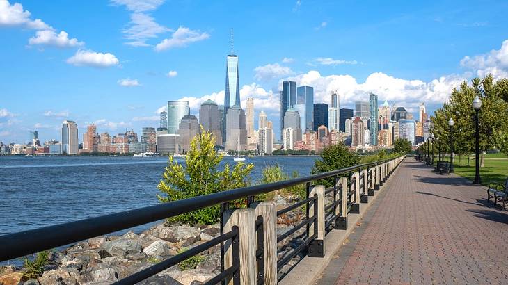 A path in a park with a river on one side and a city skyline in the distance