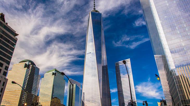 A tall mirrored skyscraper surrounded by other buildings under a cloudy sky