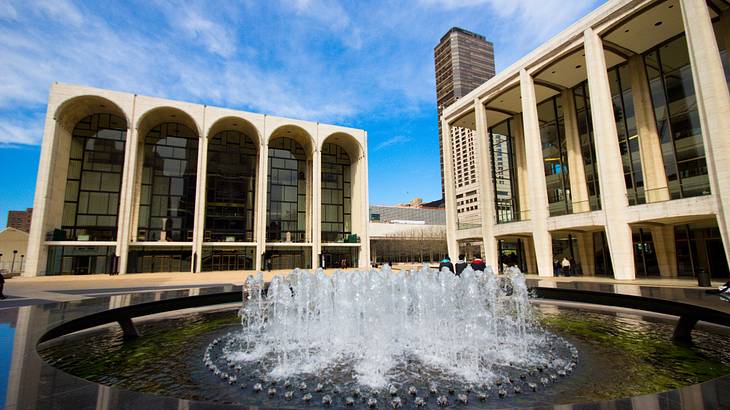 Two buildings with large arched windows and a fountain in front