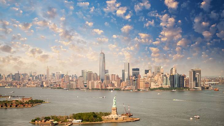 An aerial city skyline with skyscrapers and water surrounding a statue island