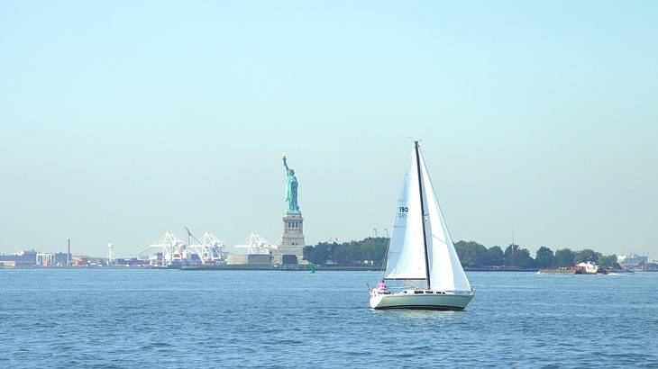 A sailboat on the water with the Statue of Liberty in the distance