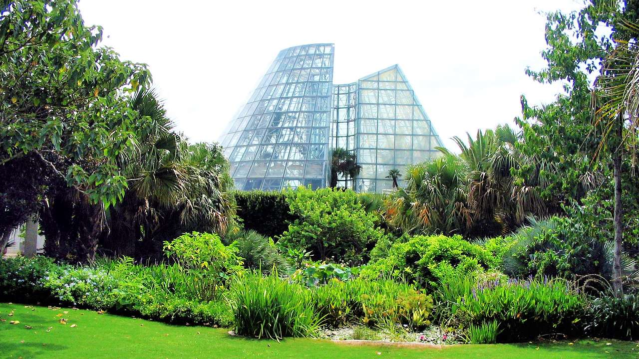 A glass-paneled cone-shaped structure with a lush landscaped garden in front