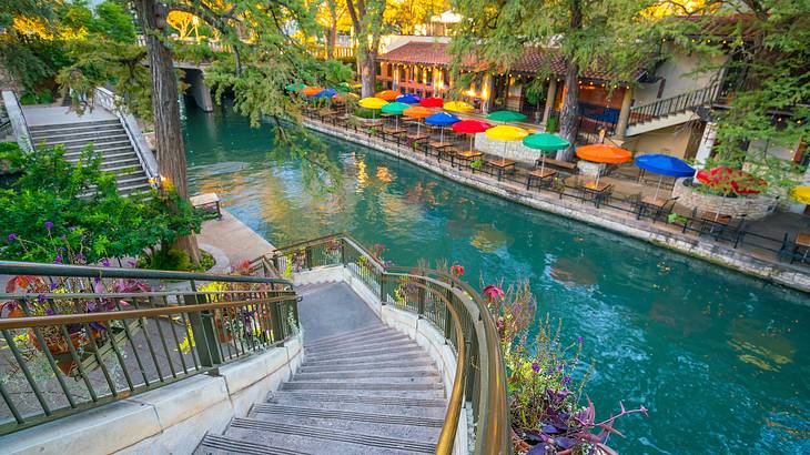 Stairs leading to a paved riverside near trees and colorful parasols