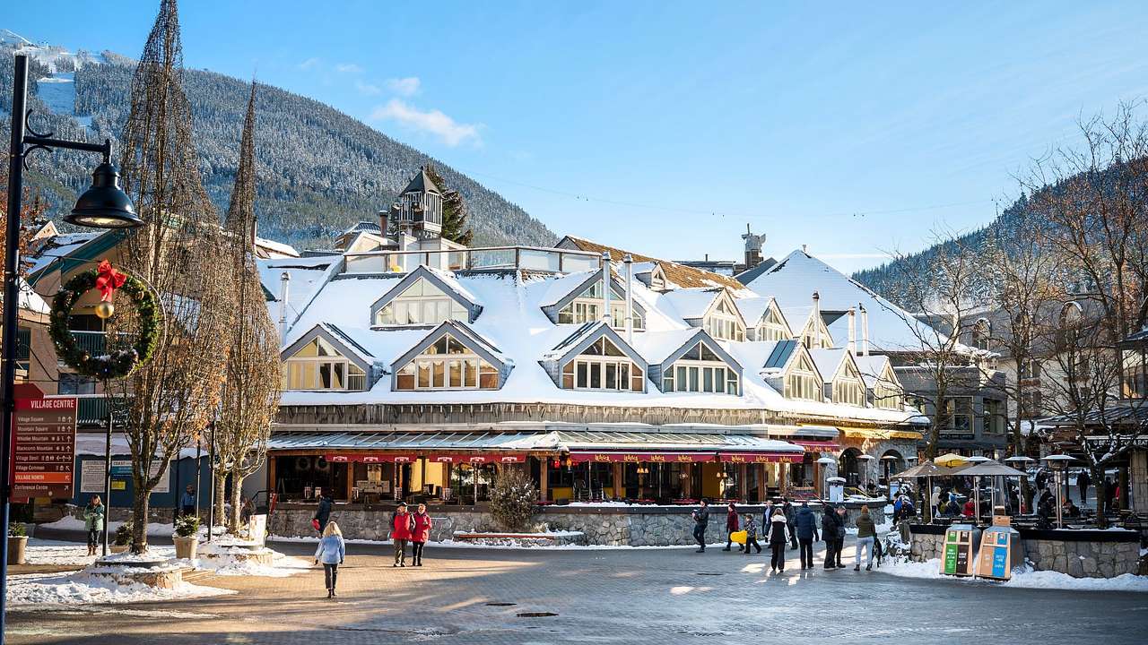A ski village with people walking next to snow-covered buildings and a mountain