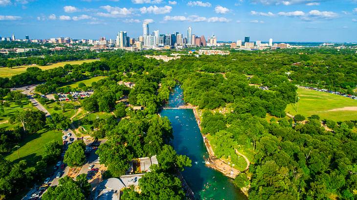 A winding body of water in the middle of groves with a city skyline at the horizon