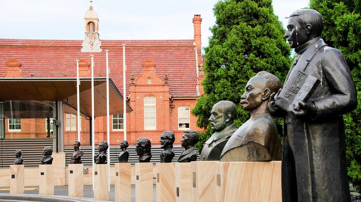 Bronze busts and a statue arranged in a circular manner near trees and a building