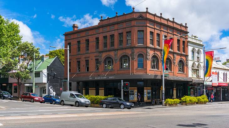 A red brick corner building with hanging flags near a road with cars