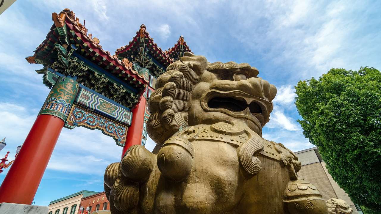 A statue of a guardian lion near a red Chinese-style arch and a tree