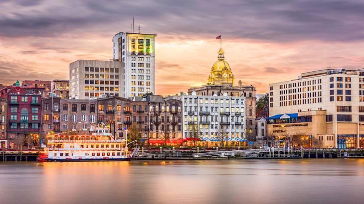 A city skyline illuminated at night next to a river with a riverboat on it