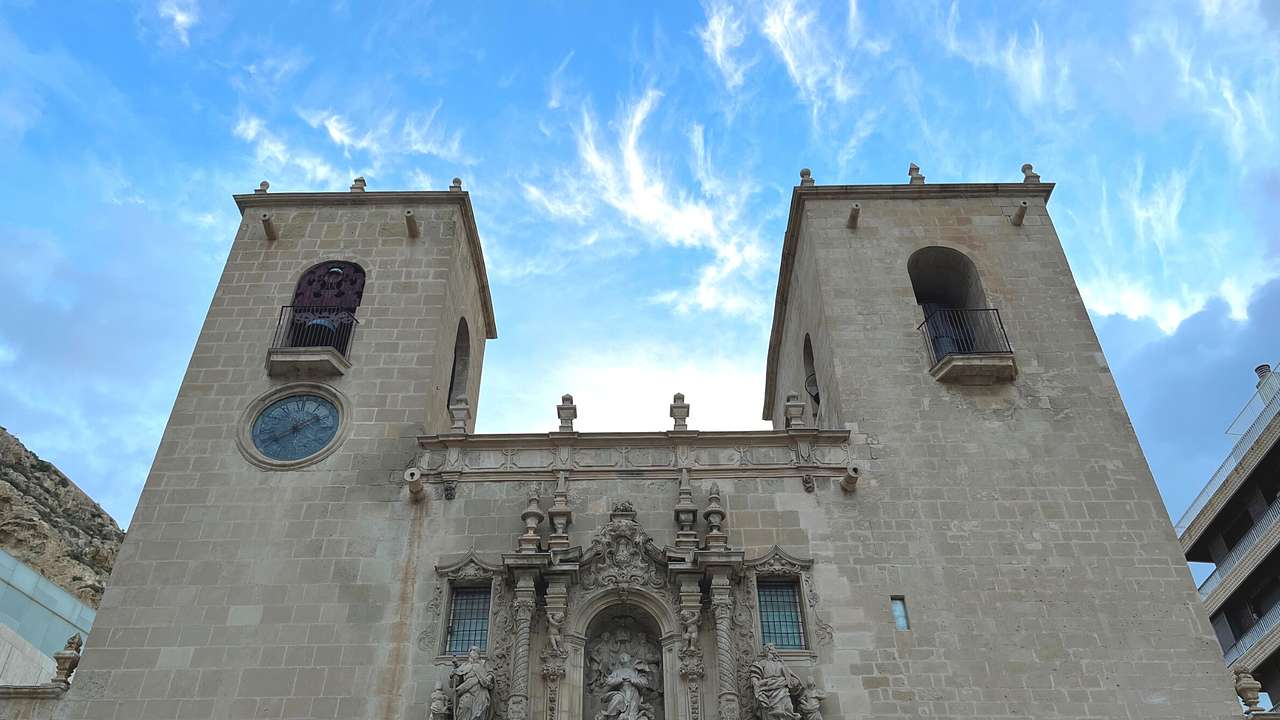 Looking up at two large stone towers of a church against blue sky
