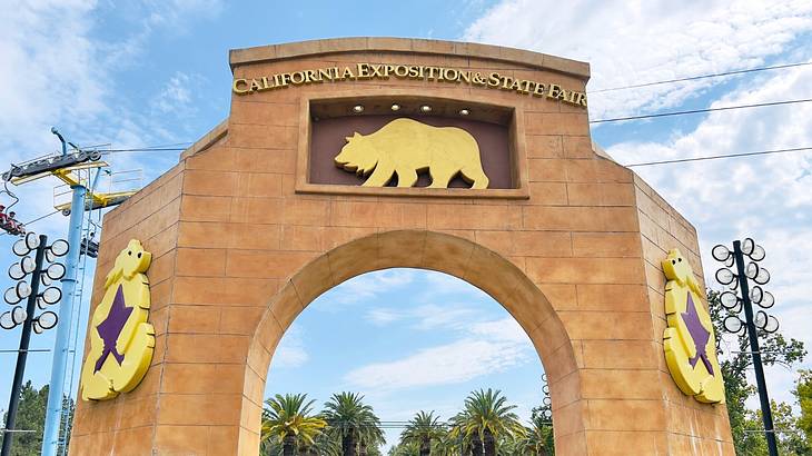 A large archway with a bear symbol and a sign on it, with trees and exhibits behind