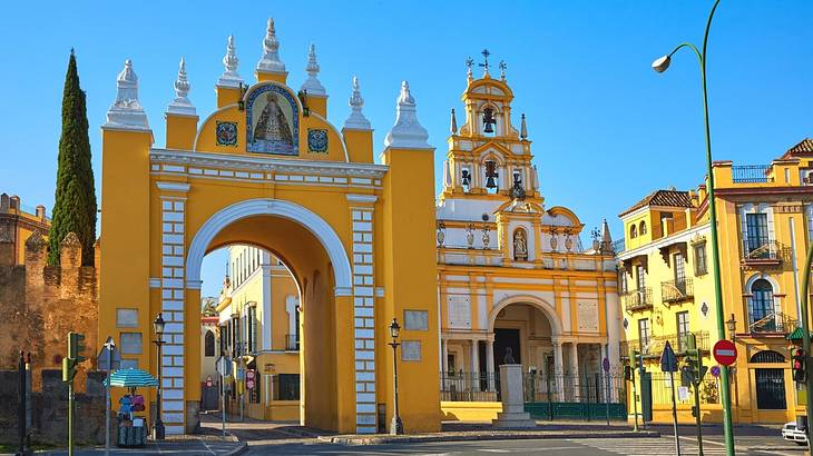 A bright yellow archway next to a white and yellow cathedral under a blue sky