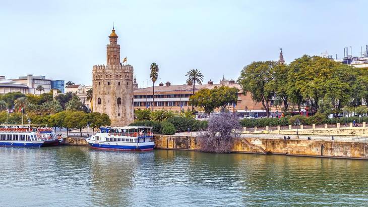 A river with two tourist boats on it, next to a stone tower and green trees