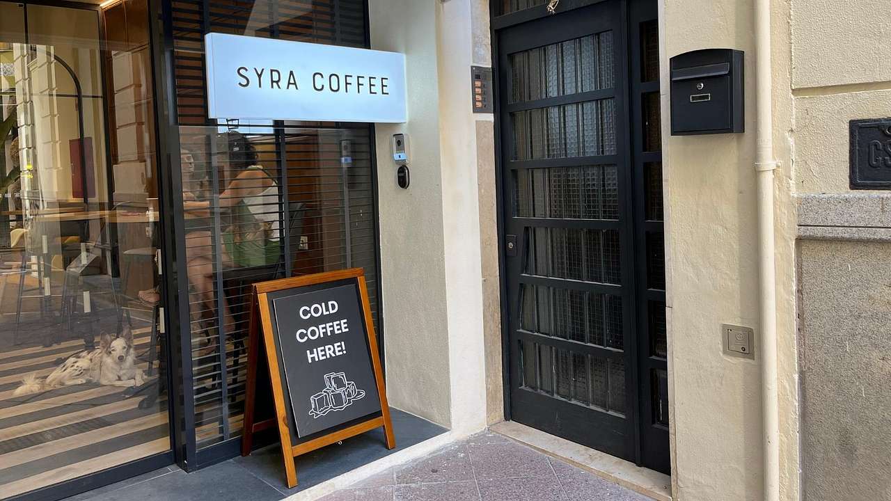 A coffee shop with a sign that says "Syra Coffee" and "Cold Coffee Here" in the entry