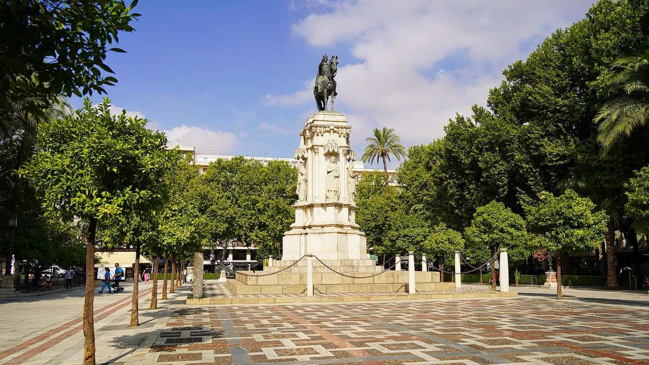 A statue of a man on a horse on top of a pillar in a square surrounded by trees