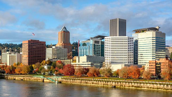 Looking towards water against bushes and buildings under a partly cloudy sky