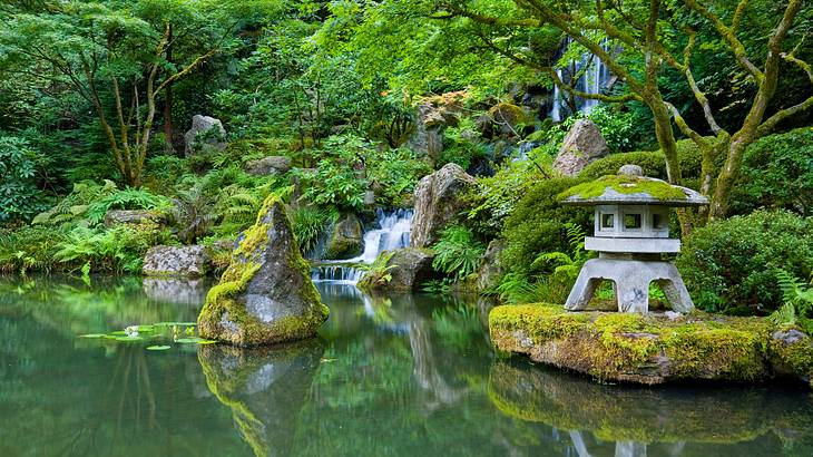 A small concrete Japanese teahouse surrounded by greenery along with a pond