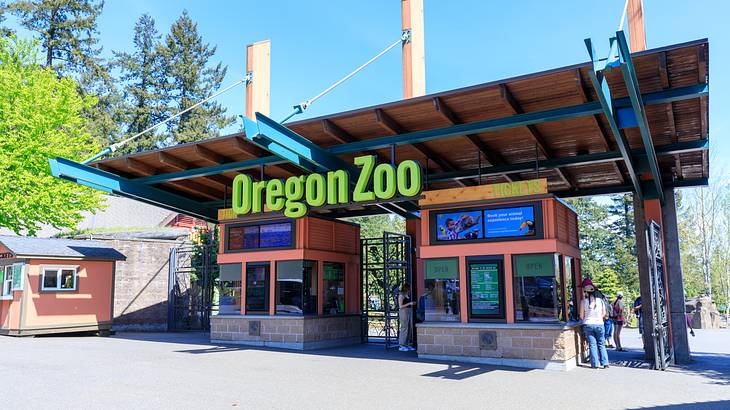 An entrance with two ticket booths and a green sign "Oregon Zoo" on a sunny day