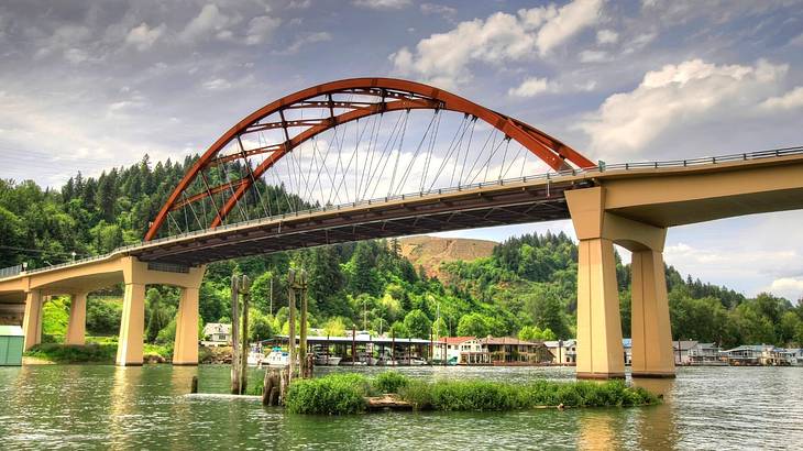 Looking towards a bridge over water against a green hill under a partly cloudy sky