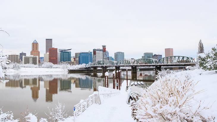 A bridge over a river with a city in the background and snow-covered terrain