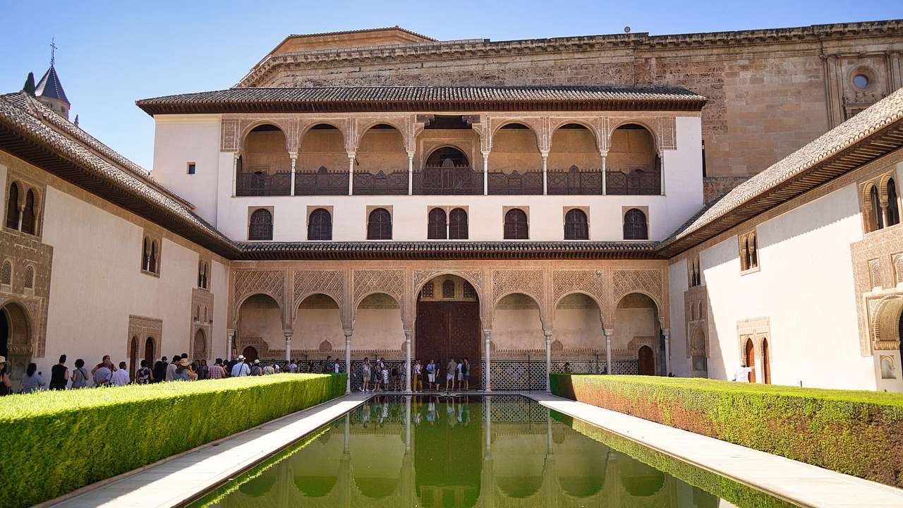 A Moorish palace with two levels of arched balconies reflecting into a green pool