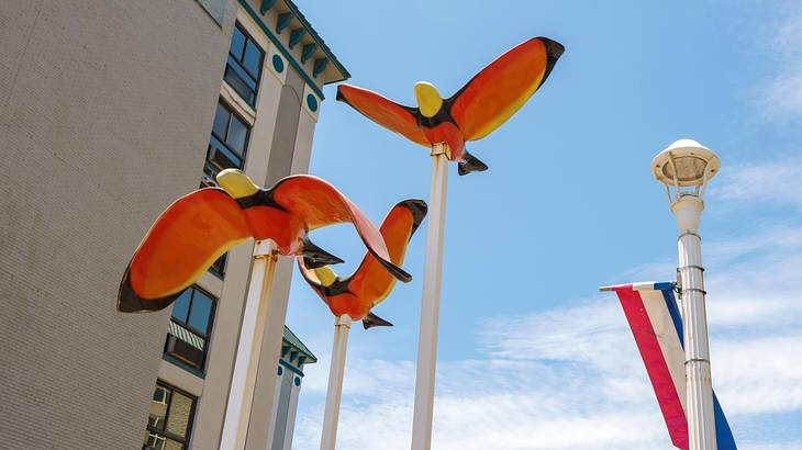An artwork of three orange and yellow birds next to a lamppost and a building
