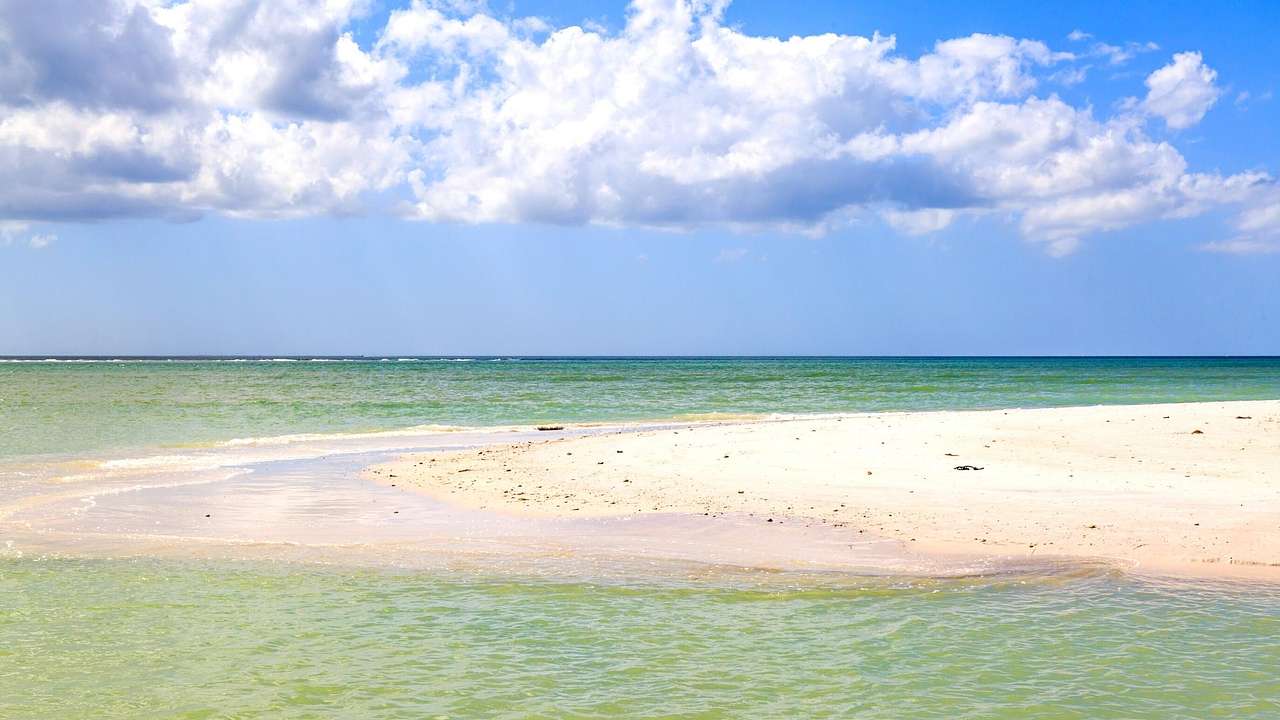 A sand bar surrounded by turquoise water under a blue sky with clouds