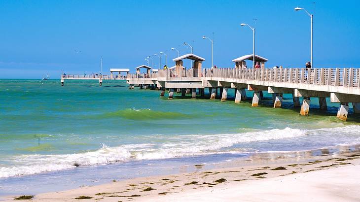 A pier stretching out into the ocean next to a sandy shore on a clear day