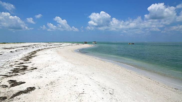 A white sand beach with a blue ocean to the side and boats in the distance