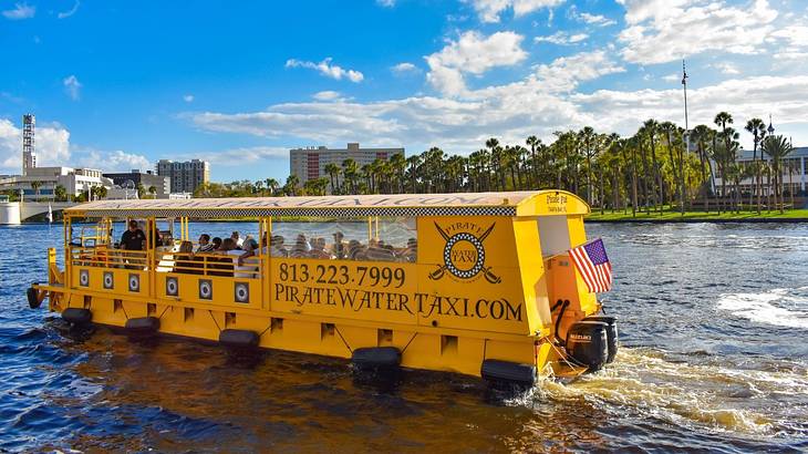 A yellow boat that says "Pirate Water Taxi" on the water with palm trees behind it