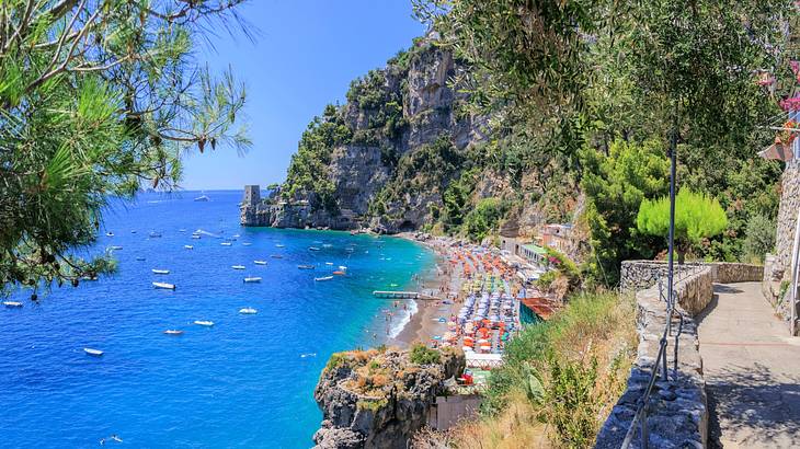 High-angle shot of a beach cove with many colorful parasols and ships