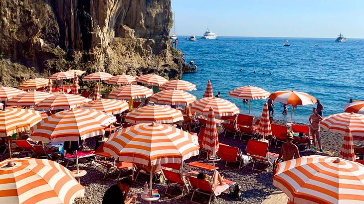 White and orange parasols by the beach shore near a rocky mountain with trees