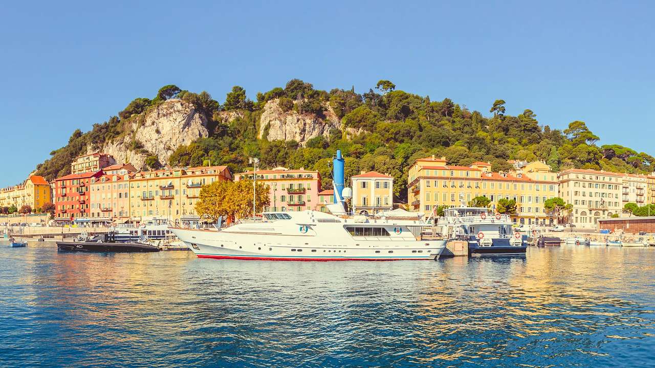 A sea with yachts by an island with colorful buildings and a mountain