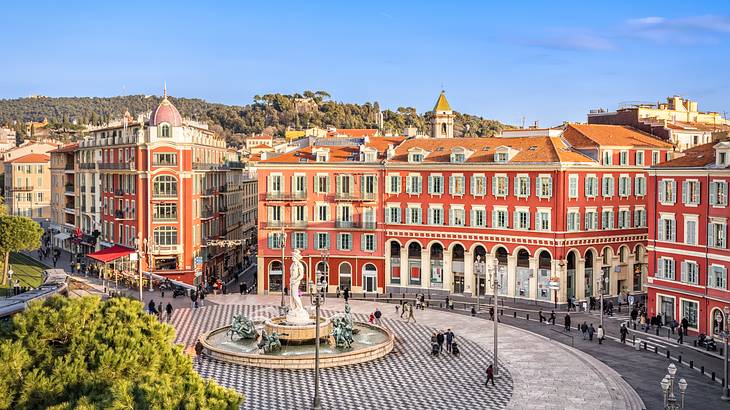 A wide circular paved space with a fountain in the middle surrounded by old buildings