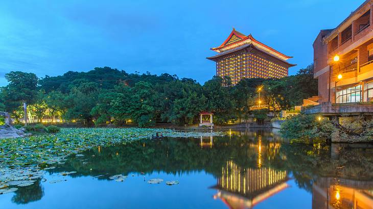 The Grand Hotel in Taipei at night behind water and green trees