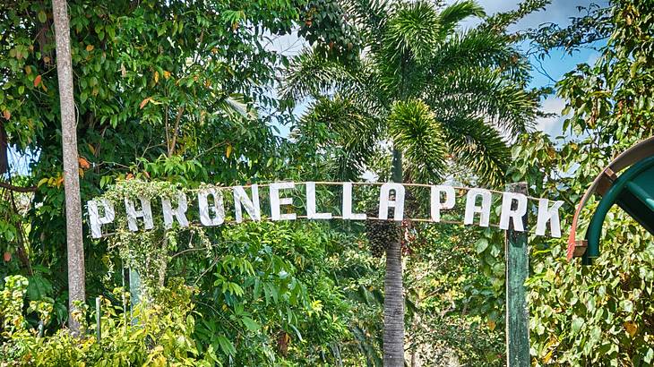 A white sign to a tropical park placed high among green trees