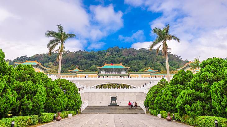 A wide walkway near trees leading to the stairs of a palace-like structure on top