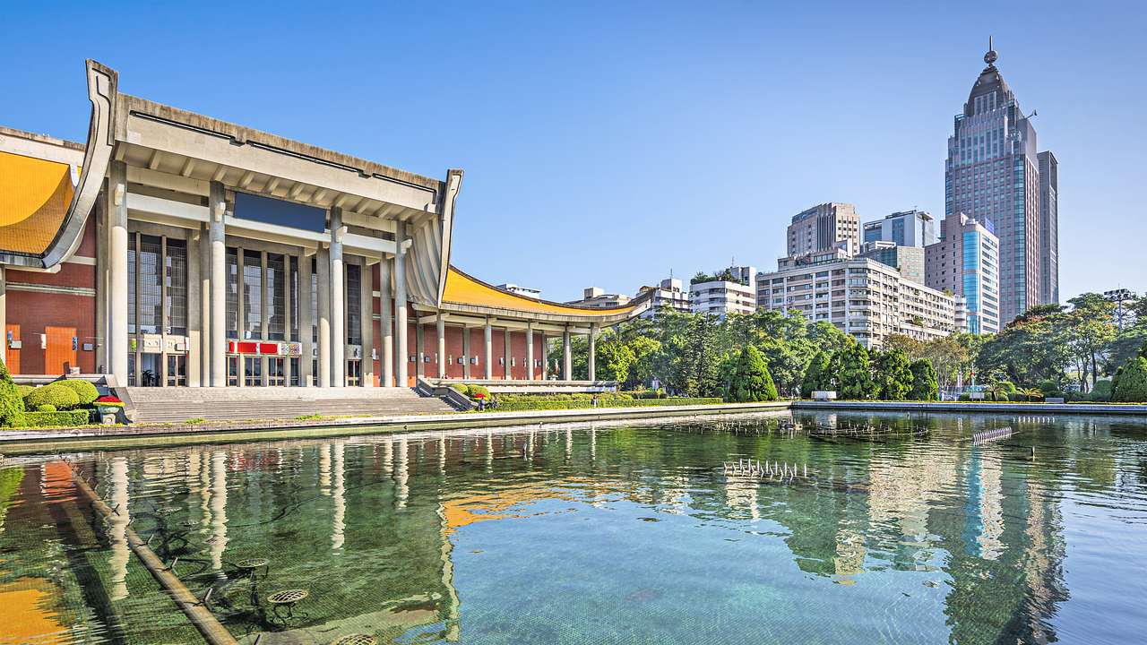 A water fountain near a Chinese palace-like building and modern skyscrapers