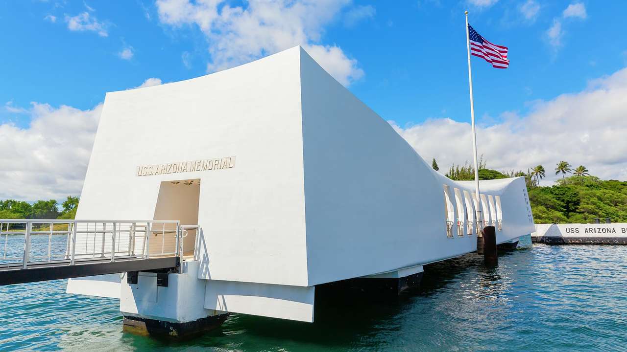 A white structure with a flag, above the water under a partly cloudy sky