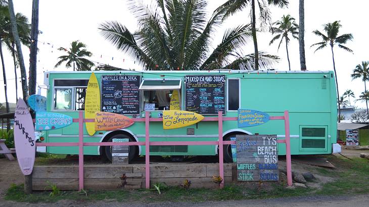 A colorful food truck next to palm trees and a fence