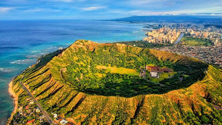 A volcanic crater filled with trees sitting amidst the sea, surrounded by buildings