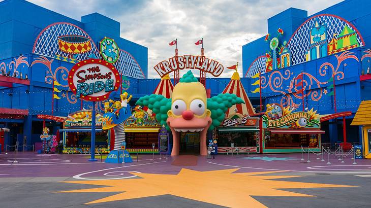 An amusement park with blue buildings, signs, and a clown face sculpture