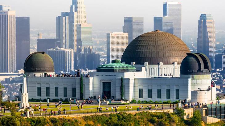 A structure with several domes next to a park with city buildings in the background