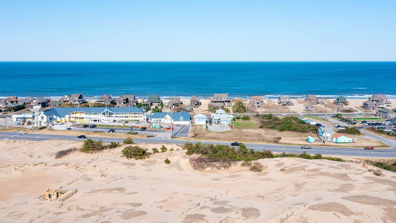 A sandy area with houses and the blue ocean in front of it under a blue sky