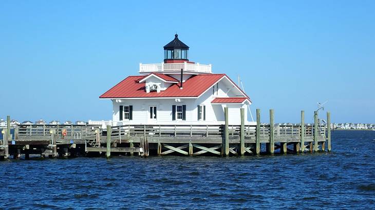 A lighthouse standing on a wooden platform surrounded by blue water and a blue sky