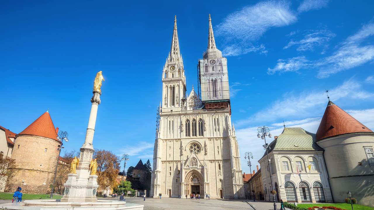 A cathedral with two spires next to buildings and a column in a square