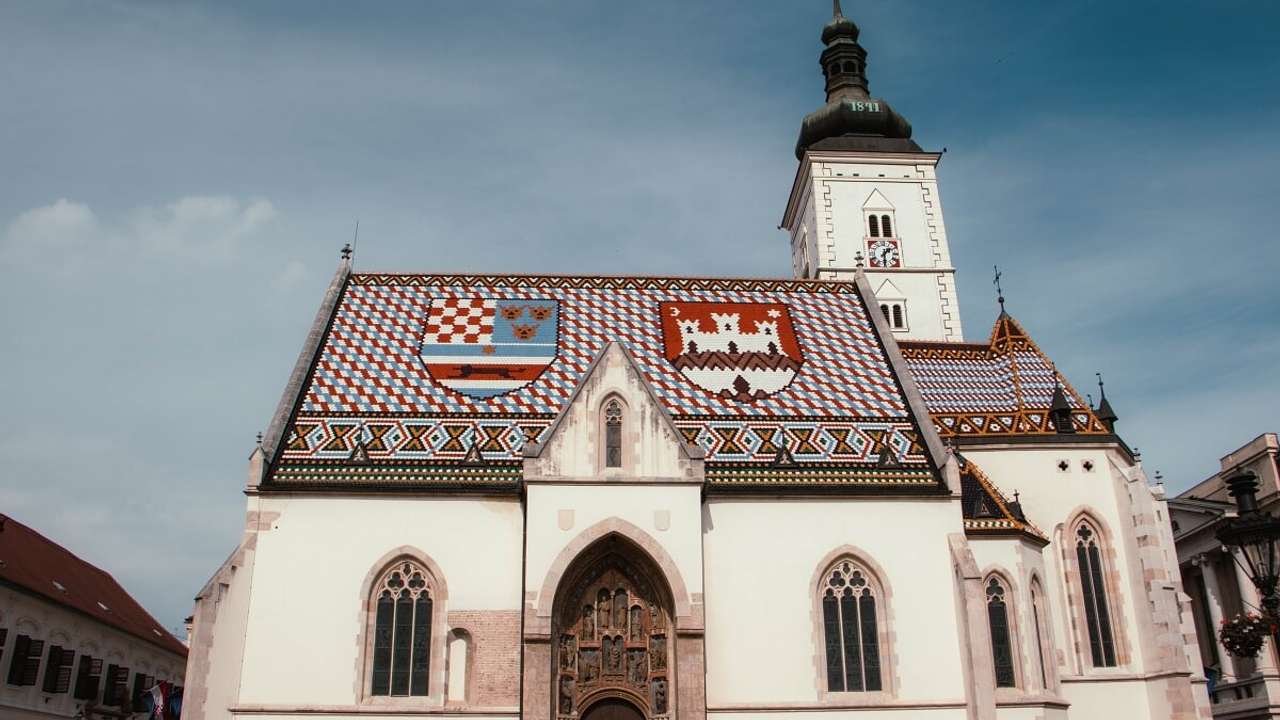 A white church with a patterned tiled roof next to a blue sky