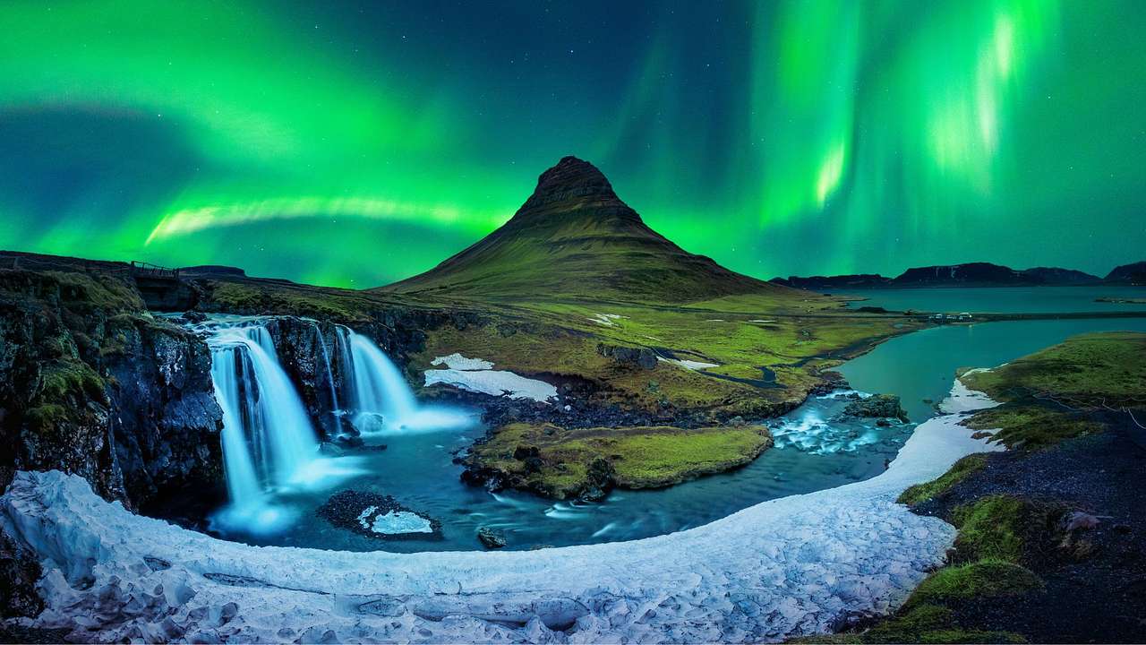 A mountain and waterfalls against the dark sky with green lights