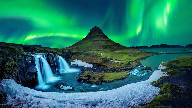 A mountain and waterfalls against the dark sky with green lights